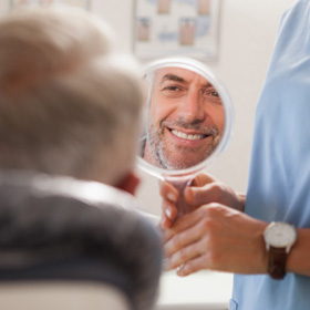 a dentist holding a mirror for a smiling patient