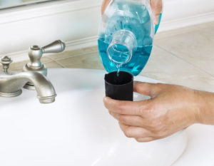 Hands pouring blue mouthwash into cap over sink