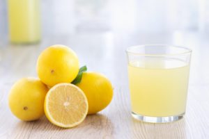 glass of lemonade next to a pile of lemons on a table 